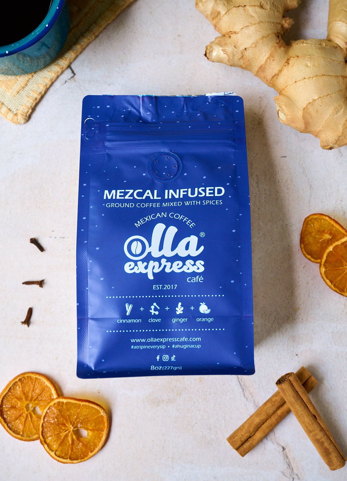 Blue Mezcal Infused coffee bag from Olla Express Cafe on a light surface with spices and oranges.