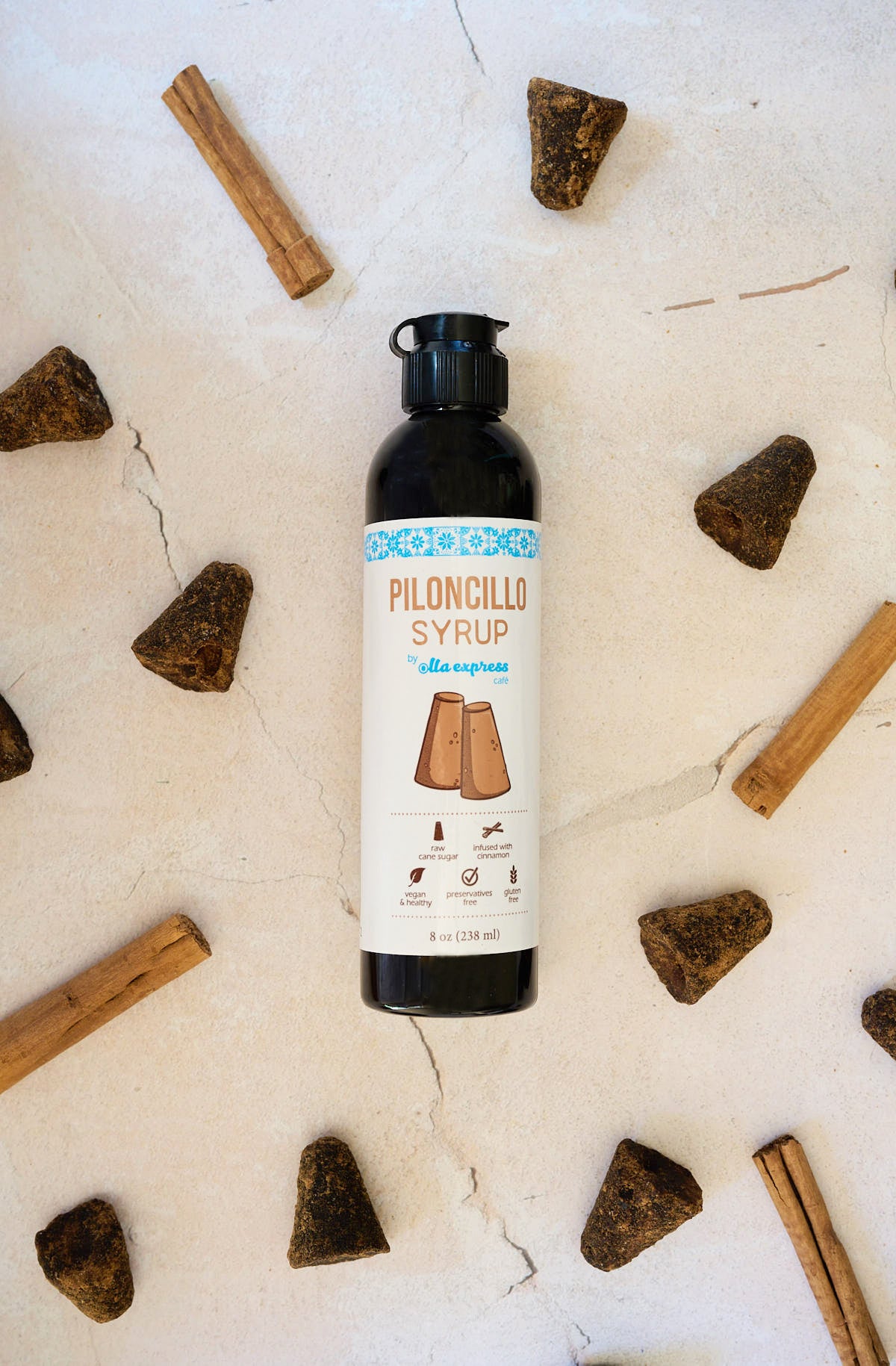 Bottle of piloncillo syrup surrounded by raw sugarcones on a light background