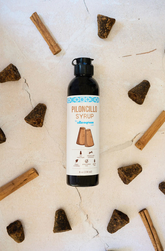 Bottle of piloncillo syrup surrounded by raw sugarcones on a light background
